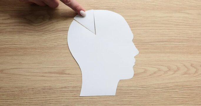Woman hand puts missing triangular piece of human head paper shape on wooden table. Missing element as psychological concept of thinking on wooden board