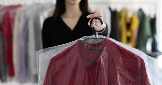 Female manager of dry cleaning holds red men shirt standing in company office. Brunette employee offers client to pick up clean clothes slow motion