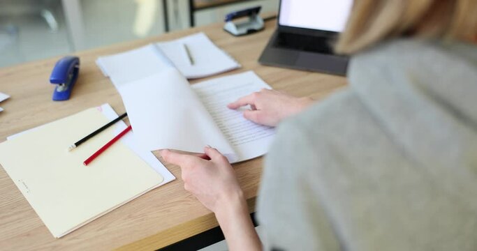 Female hands carefully open paper folder with film script. Actress looks for own role lines. Script lies on wooden office desk with pens and contract slow motion
