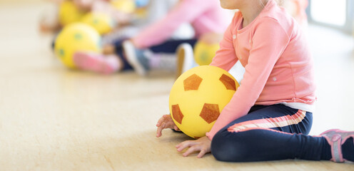 Children in kindergarten at soccer class. Little girl with foam soccer football balls sitting in line and playing game. Sports soccer training at kindergarten