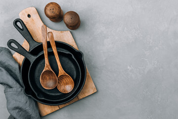 Empty pans. Cast iron pans with wooden spoons on gray stone background, top view, copy space.