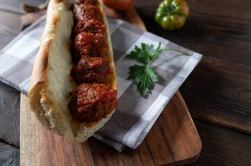 Meatball sandwich with tomato sauce and melted mozzarella cheese on wooden table.