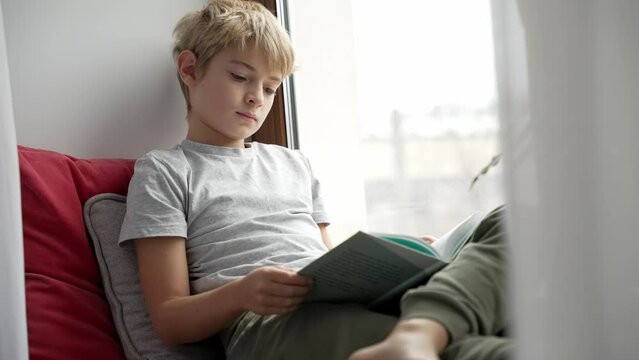 Boy is reading a book. Teenager sitting next to window at home alone and is reading and thinking about something. Emotional concept. 