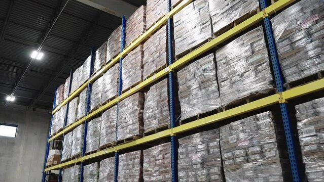 tracking shot of product inventory in warehouse stacked on shelves, pallets, plastic wrapped rows high to the ceiling in a warehouse