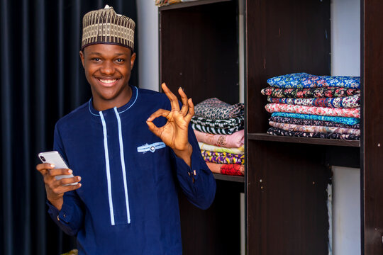 young good looking african man in african attire, operating his phone happily