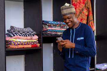 young good looking african man in african attire, operating his phone happily