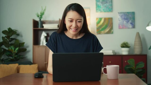 Happy Attractive Young Asian Woman Using Laptop Talk Video Conference Call With Friends Or Family. Beautiful Female Smile Looking At Laptop Computer Screen Talking Sit At Desk In Living Room