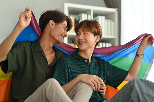 Image of gay couple embracing under LGBT pride flag. LGBT, love and human rights concept