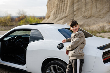 Teenager boy stand near white muscle car. Young teen driver.