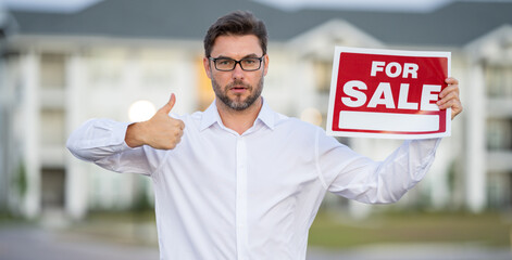 Handsome real estate agent holding banner house for sale. House with land and insurance. Business man real estate agent in business suit presenting the house for sale. Land agent trying to sell house.