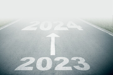 2023 to 2024 text on asphalt road with white arrow sign on road goes into fog. Direction way sign....