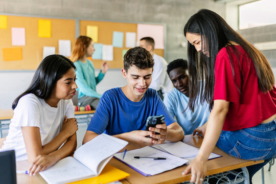 Multiracial group of student friends watching social media content on smartphone during the break in college classroom - Powered by Adobe