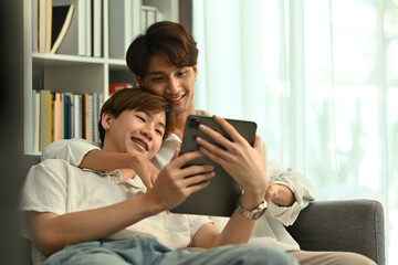 Passionate young gay couple relaxing on couch and browsing internet on digital tablet. LGBT, love and lifestyle concept