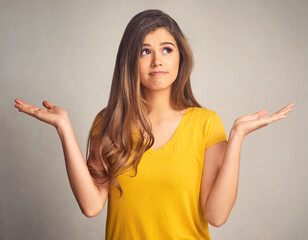 Thinking, doubt and shrug with a woman in studio on a gray background looking confused by her options. Idea, question and hand gesture with an attractive young female person weighing up a decision