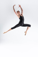 Fototapeta na wymiar One Caucasian Ballet Dancer Young Athletic Man in Black Suit Posing Dancing in Studio On White.