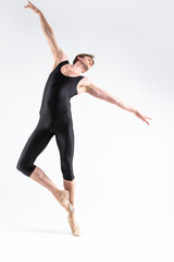Fototapeta premium One Caucasian Ballet Dancer Young Athletic Man in Black Suit Posing in Stretching Pose Studio On White.