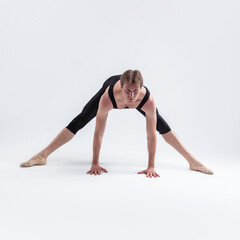 Fototapeta na wymiar Ballerino Dancer Sitting While Practising Waist and Body Stretching Exercices With Lifted hands In Black Sportive Tights in Studio.