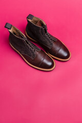 Upper View of Pair of Premium Dark Brown Grain Brogue Derby Boots Made of Calf Leather with Rubber Sole Placed On Pink Background.