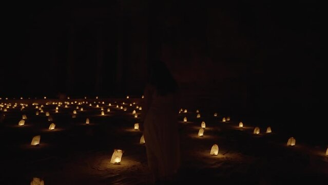 Camera orbits young woman near Petra Treasury facade at night, candles