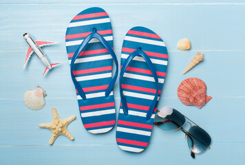 Flip flops with sunglasses and airplane on wooden background, top view