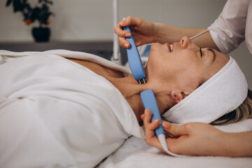 A cosmetologist makes a microcurrent facial therapy to a woman in a beauty salon.