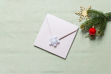 Christmas still festive life. Blank invitation mockup, envelope on textile background. Fir branches, wooden snowflake, red christmas ball on the table. Copy space, top view.
