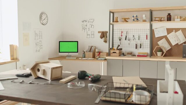 Interior of woodworking workshop with birdhouse and drills on workbench, computer with green screen and shelves in background, no people there