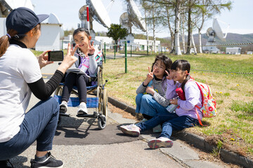 車いすに乗った女の子と学校の遠足に行く小学生の友達 - obrazy, fototapety, plakaty