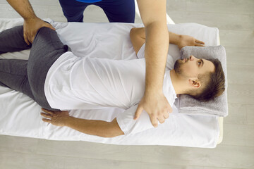 Young male osteopath is working on the spinal lumbar region of young patient to align the...