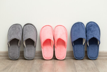 Three pairs of home slippers near the white wall. Shoes for home usage concept