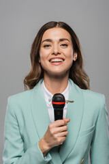 Portrait of smiling brunette event host in blue formal wear talking at wireless microphone and...