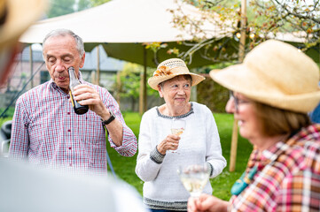 Group of different elderly people sipping wine and beer, preparing a lunch and an outdoor party in the garden, healthy and happy elderly people concept