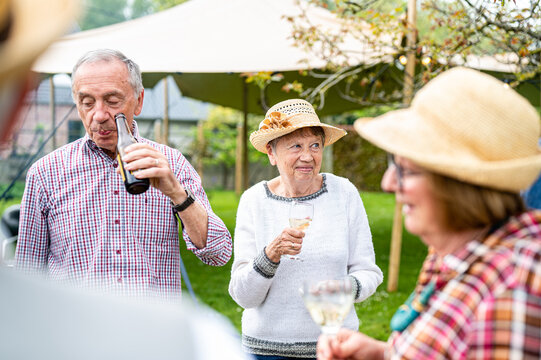 Group of different elderly people sipping wine and beer, preparing a lunch and an outdoor party in the garden, healthy and happy elderly people concept