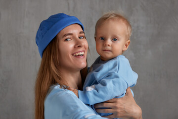 Close-up portrait of a happy young mother and baby infant in her arms. Mom hugs her cute baby. Baby and mother in the same blue clothes. Family love and harmony.