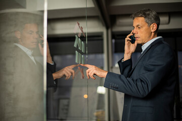 Portrait of successful businessman in office. Man writing on the glass board in office. Businessman talking to the phone.