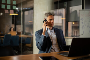 Businessman in office. Handsome man talking on phone at work..