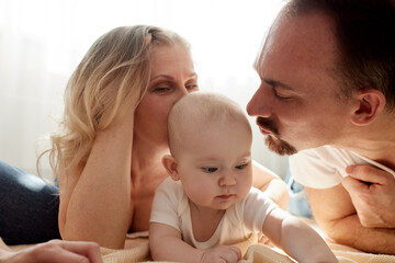 Loving grandma and dad hug and kiss their baby on the floor in the children's room. Happy loving family. Parents and child smile happily.