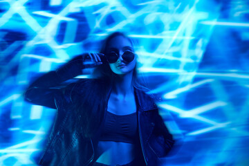 Unfocused portrait of young beautiful girl in leather jacket posing over blue background with...