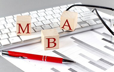 MBA written on a wooden cube on the keyboard with chart on grey background