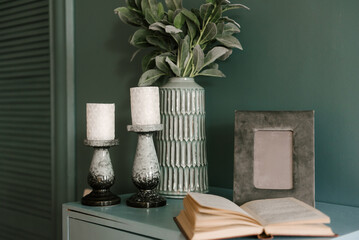Modern interior in emerald color with decor candles, book, vase with flowers