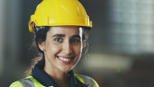 Portrait smiling hispanic latin beautiful female engineering worker in yellow safety suit and hardhat, Technician woman industrial worker standing in factory workplace.