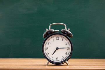 Alarm clock on wooden table on blackboard background in classroom