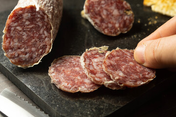 Man takes a slice of fresh Italian salami