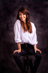 Obraz na płótnie Canvas Studio portrait of a brunette haired attractive woman wearing white shirt and black jeans while posing at isolated dark background