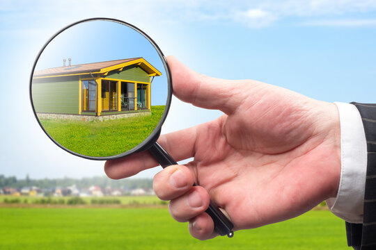 Realtor hand. House under magnifying glass. Real estate. Finding place to build cottage concept. Template for real estate agency. Selection of places for house. Realtor hand near green lawn.