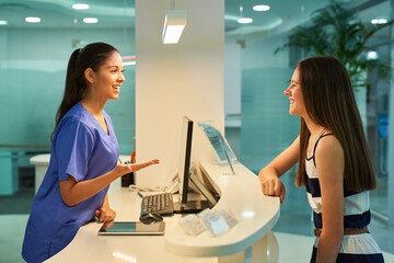 Medical, reception and nurse with patient in hospital for advice, help and information. Medicine, happy and healthcare with women at desk in clinic for nursing, waiting room and service - obrazy, fototapety, plakaty