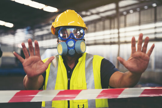 Chemical specialist wear safety uniform and gas mask showing his hands signal no entry chemical dangerous area in the industry factory while standing behind line area barrier red and white colour