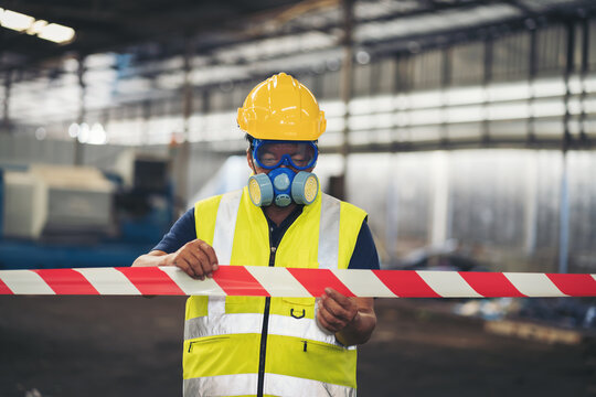 Chemical specialist wear safety uniform and gas mask showing line symbol signal no entry chemical dangerous area in the industry factory while standing behind line area barrier red and white colour