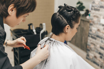 hairdresser makes a haircut to a woman in the salon. The hairdresser cuts wet hair, combing with a comb. client with short hair. back view