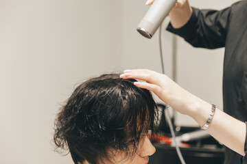 Naklejka premium Close-up of the hands of a hairdresser drying women's hair with a hairdryer. short haircut and styling